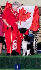 A person in red clothing stands with a black and white dog on a podium with a Canadian flag in the background.