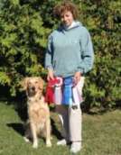 A person stands outside with a Golden Retriever, holding several award ribbons.